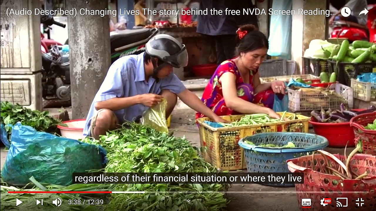 Screenshot from "Changing Lives: The story behind the free NVDA screen reader".  People in a market in Vietnam, subtitle text "regardless of their financial situation or where they live".