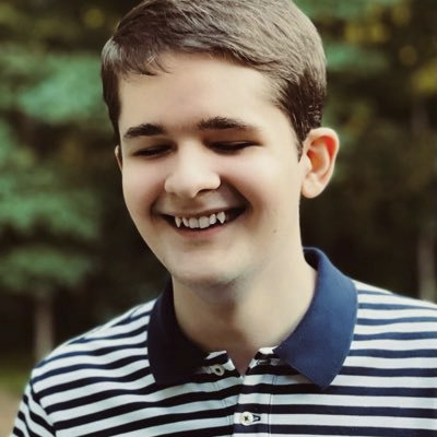 Bill Dengler, photo from Twitter profile of Bill in a blue & white striped shirt against a green leafy background